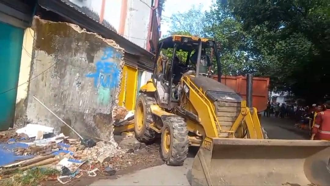 Alat berat berwarna kuning merobohkan bangunan lapak di kawasan Jalan Bandang, Makassar, dengan puing-puing berserakan di sekitarnya.