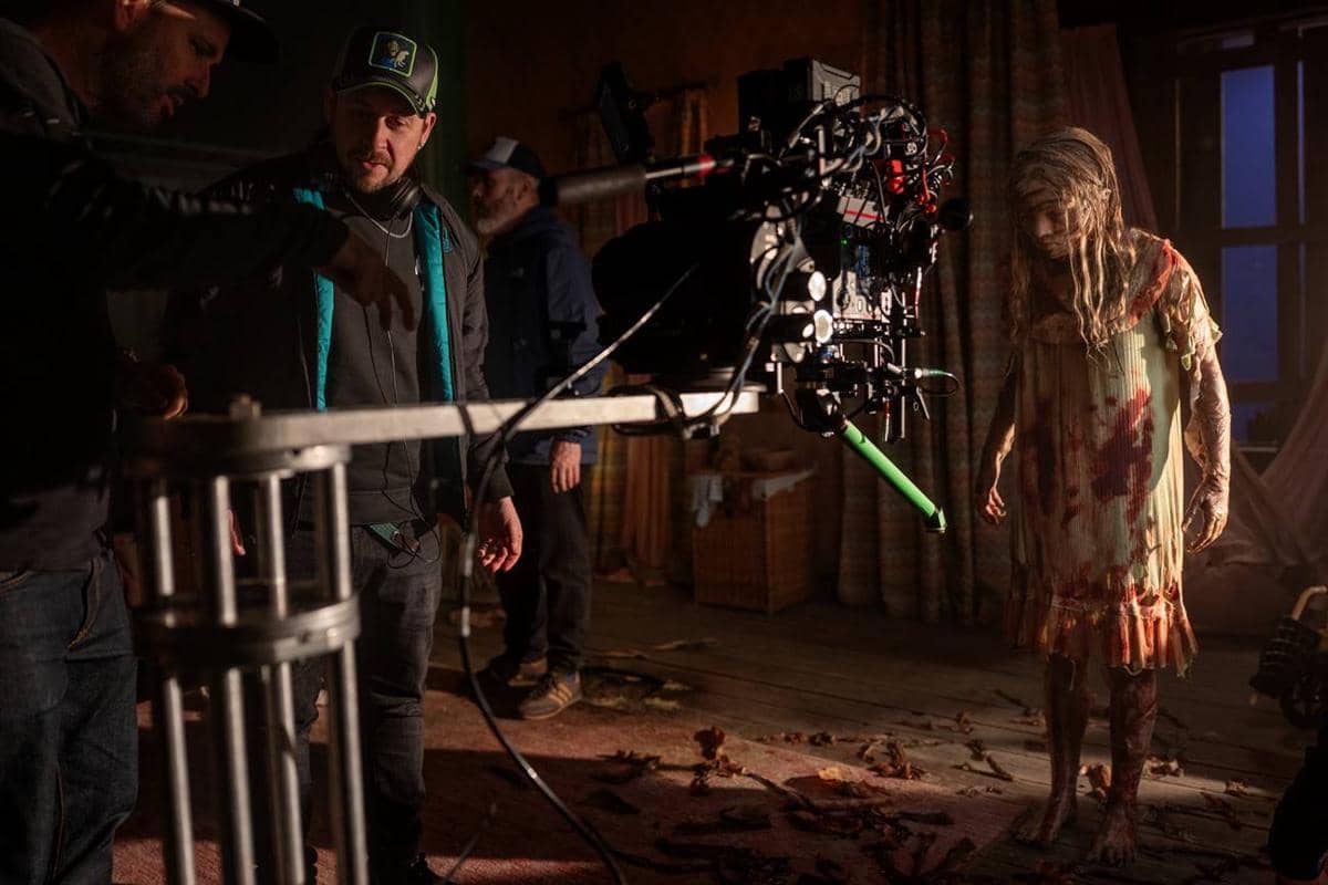 Sutradara dan kru film sedang mengarahkan adegan dengan kamera besar di lokasi syuting, menampilkan aktor berpenampilan menyeramkan berlumur darah.