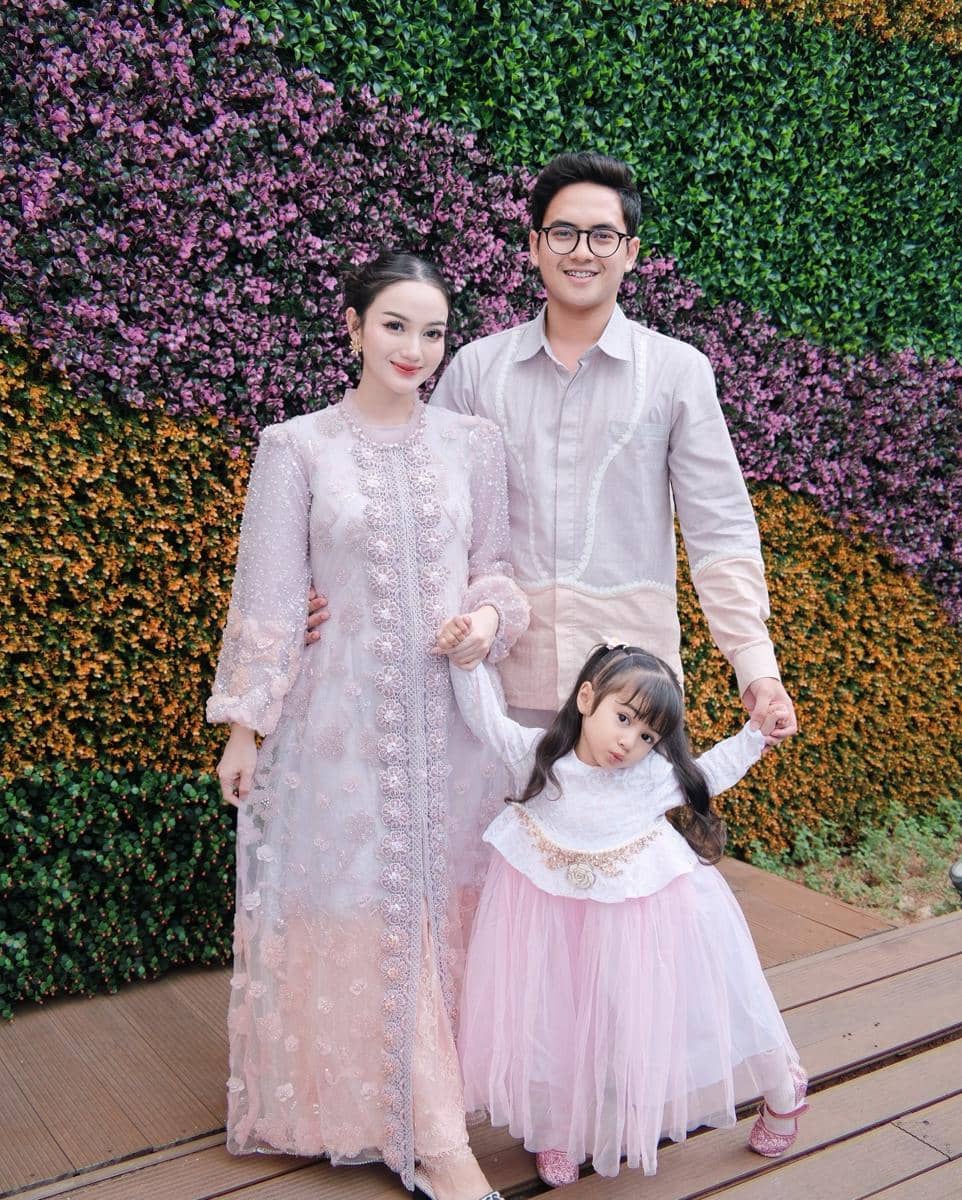 Keluarga Nanda Arsyinta mengenakan busana serasi bernuansa pastel di depan dinding tanaman hias berwarna ungu dan hijau.