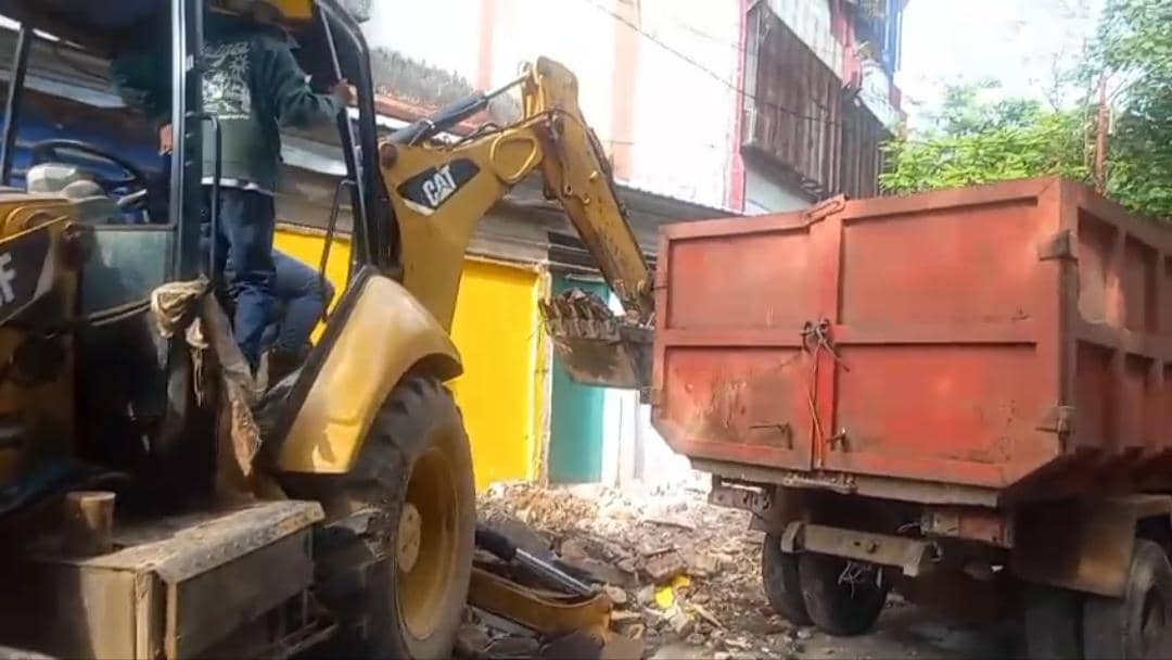 Alat berat jenis backhoe mengangkut puing hasil pembongkaran lapak PKL di Jalan Bandang, Makassar, ke dalam truk merah besar.