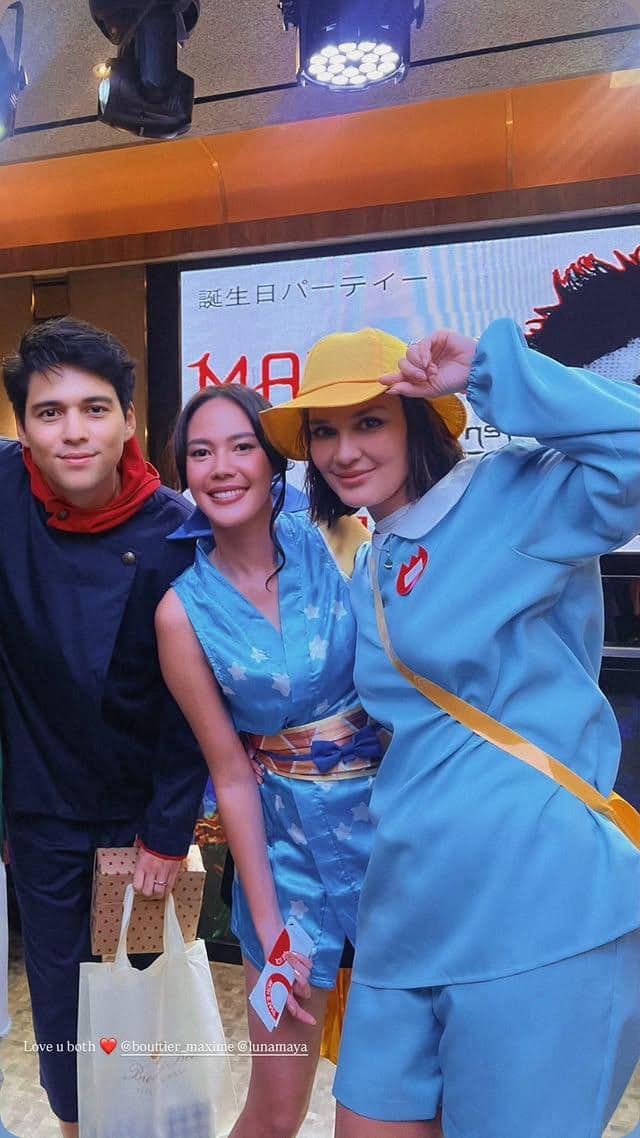 Tiga orang berpakaian cosplay anime berpose bersama di acara ulang tahun dengan latar belakang bertuliskan huruf Jepang dan nama Maxime Bouttier.