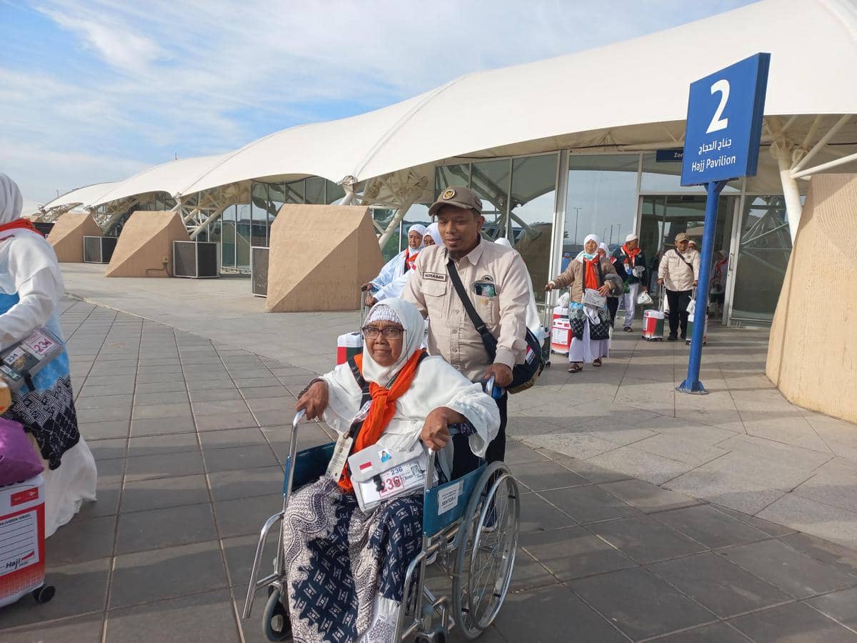 Petugas PPIH mendorong kursi roda berisi jemaah haji lansia di area Hajj Pavilion bandara sebelum menuju bus keberangkatan.