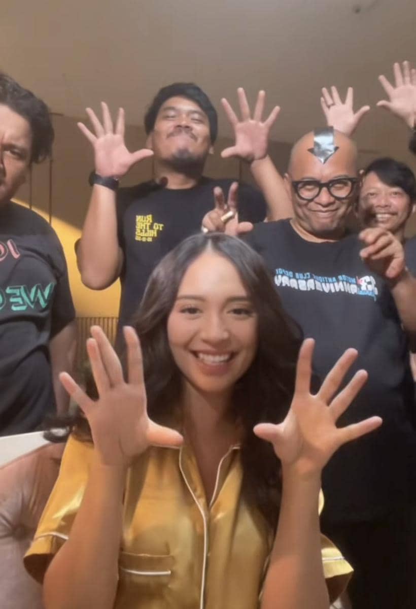 Seorang wanita tersenyum mengenakan piyama kuning berpose lucu bersama beberapa kru di lokasi syuting sinetron Terikat Janji.