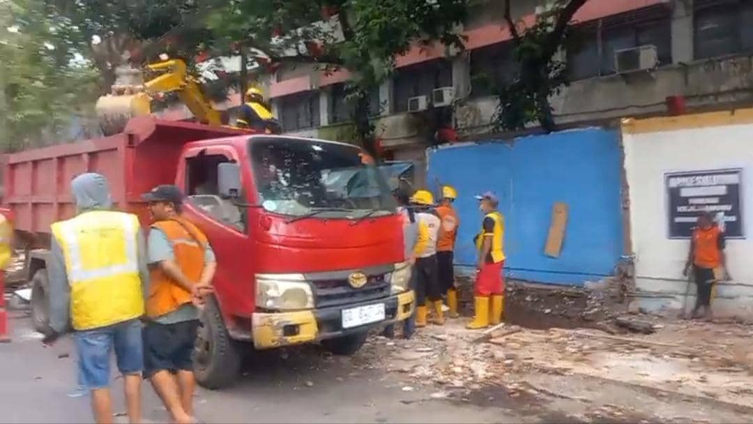 Petugas berseragam oranye dan kuning menggunakan truk merah untuk membongkar lapak PKL di kawasan Jalan Bandang, Makassar.