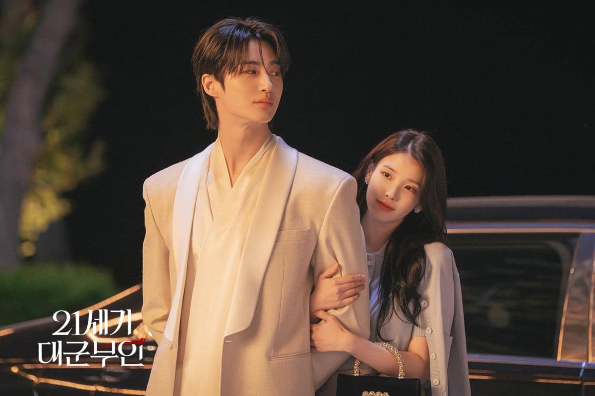 Dua pemeran drama Perfect Crown berdiri bersama di malam hari, mengenakan busana elegan dengan latar mobil hitam berkilau.