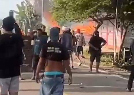 Sejumlah warga berkumpul di jalan saat terjadi bentrokan di Walenrang, Luwu, Sulawesi Selatan, dengan latar belakang api dan asap.