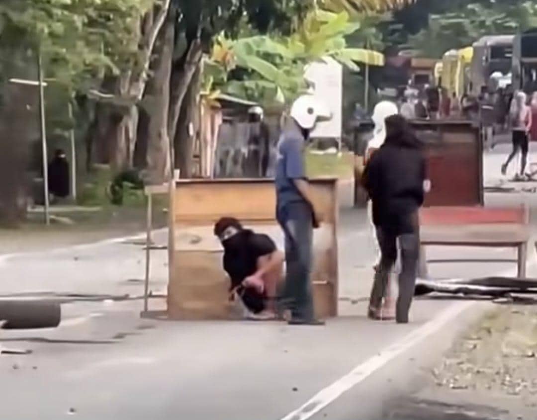 Beberapa warga mengenakan penutup wajah dan helm berdiri di jalan dengan barikade kayu saat konflik di Walenrang, Luwu, Sulawesi Selatan.