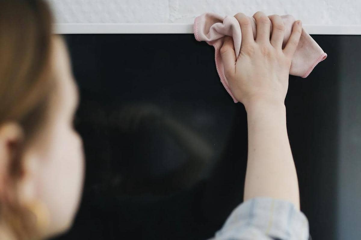 Seseorang membersihkan layar televisi LED dengan kain lembut berwarna merah muda untuk memastikan layar tetap bersih dan kering.