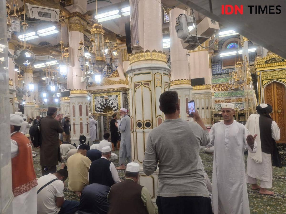 Jemaah mengenakan pakaian ihram dan gamis sedang berfoto serta beribadah di area Raudhah dengan dekorasi emas dan pilar megah.