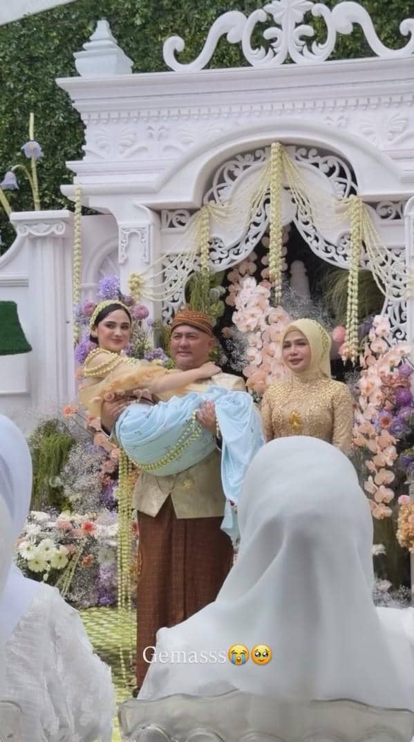 Seorang pria mengenakan pakaian adat Jawa menggendong seorang wanita dalam balutan busana tradisional di acara pengajian dan siraman.