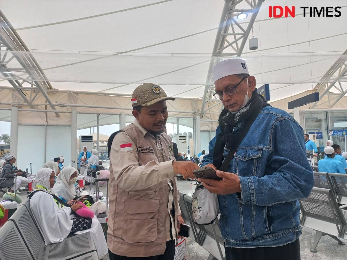 Petugas PPIH Arab Saudi membantu seorang jemaah haji memeriksa informasi di ponsel di area tunggu yang dipenuhi jemaah lain.