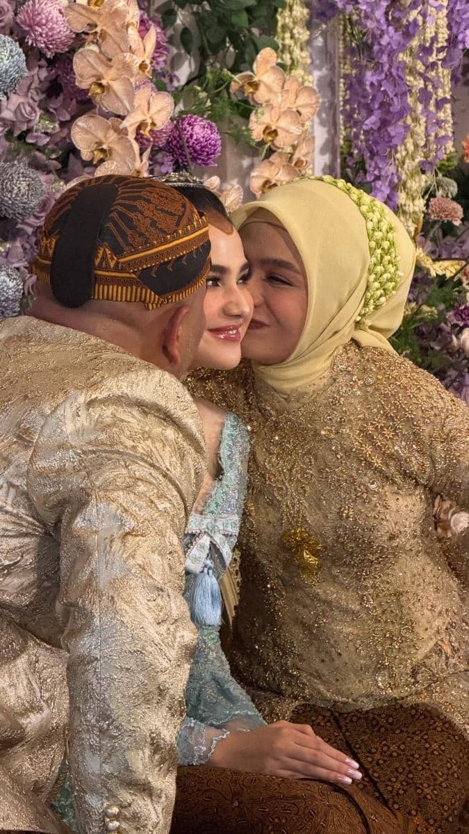 Syifa Hadju mengenakan kebaya biru muda tersenyum diapit dua orang berpakaian adat Jawa berwarna keemasan dalam acara pengajian dan siraman.