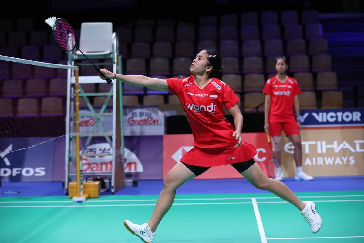 Pemain bulu tangkis putri Indonesia mengenakan seragam merah sedang berlatih dan mengembalikan shuttlecock di lapangan indoor.
