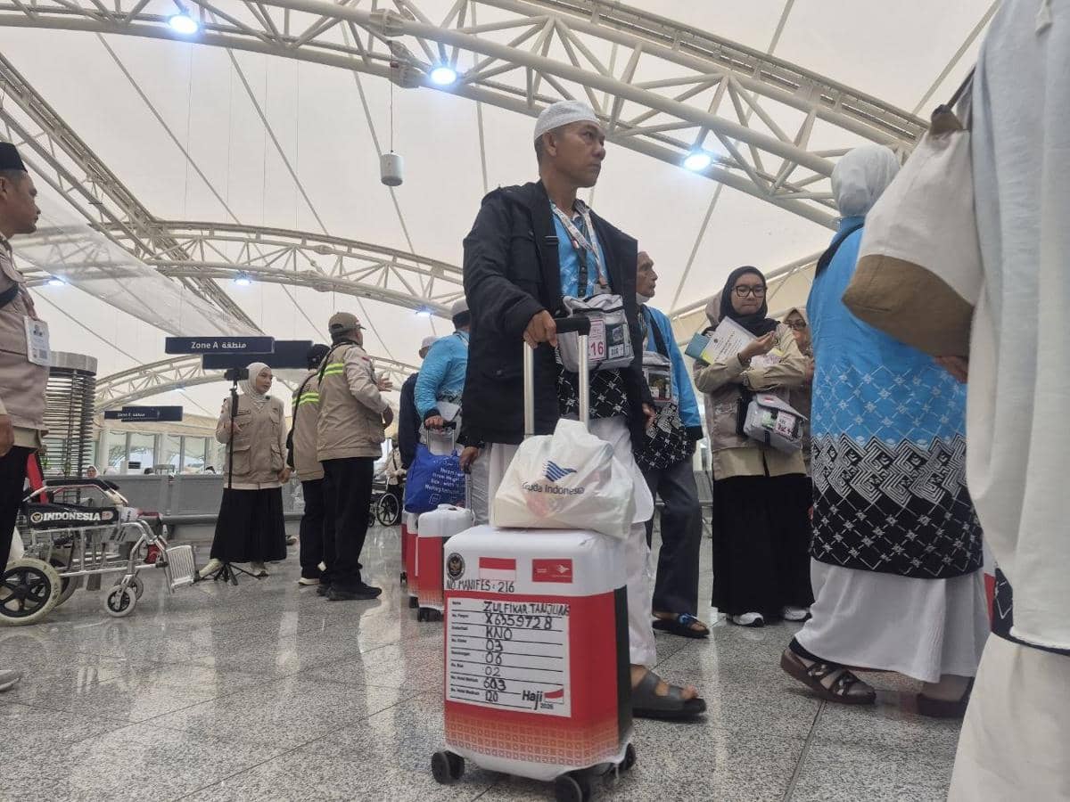 Sejumlah jemaah haji asal KNO 3 mengenakan pakaian ihram dan membawa koper kecil saat bersiap menuju bus di area pemberangkatan.