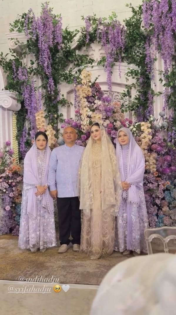 Empat orang berpose di depan dekorasi bunga ungu dan krem pada acara pengajian dan siraman menjelang pernikahan.