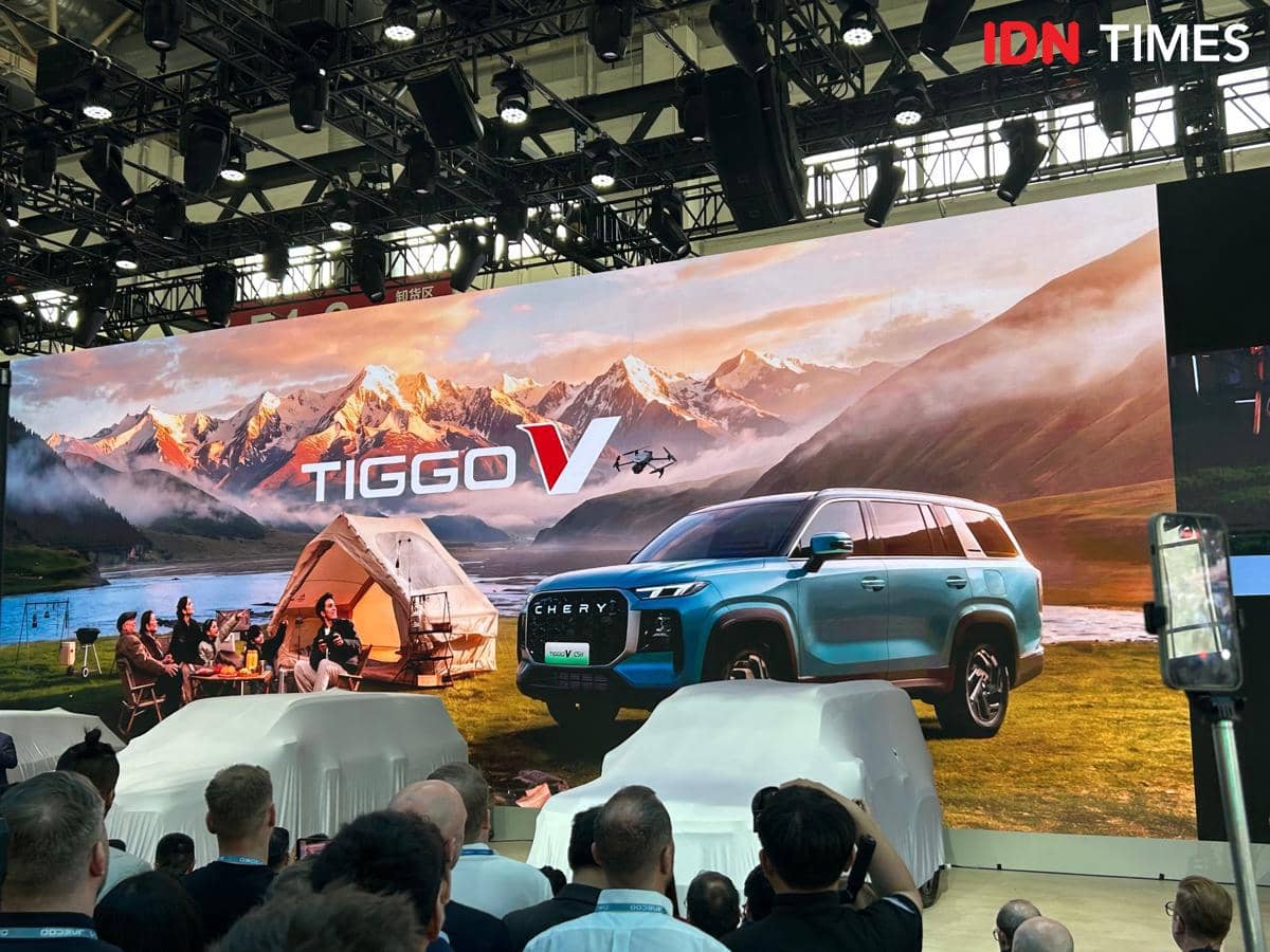 Pameran mobil Chery Tiggo V dengan latar pegunungan dan tenda di layar besar, disaksikan oleh banyak pengunjung di sebuah acara otomotif.