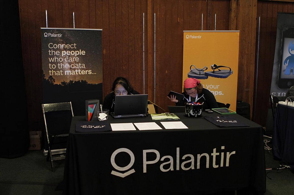 Dua orang duduk di meja booth Palantir dengan laptop di depan mereka pada sebuah acara teknologi tahun 2012.