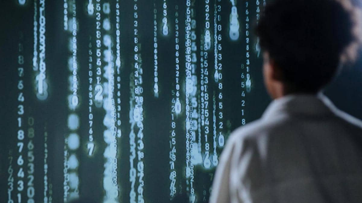 Seseorang melihat layar berisi deretan angka digital berwarna hijau yang menggambarkan aktivitas peretasan komputer.
