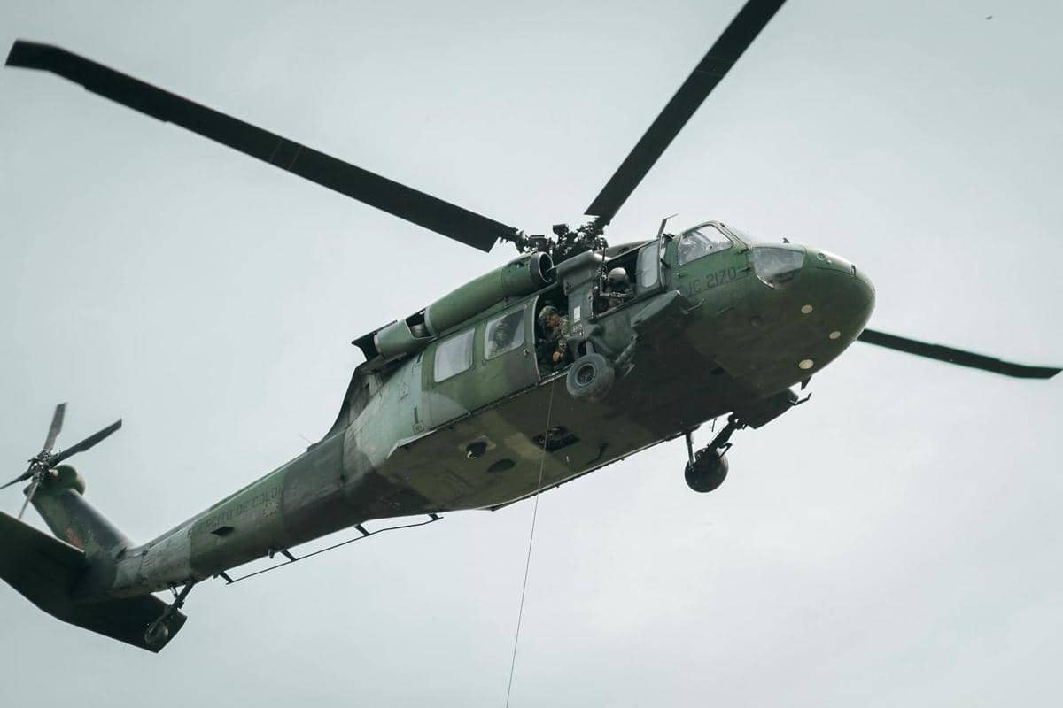 Helikopter militer berwarna hijau terbang di langit dengan prajurit di dalamnya dan tali tergantung dari bagian bawah pesawat.