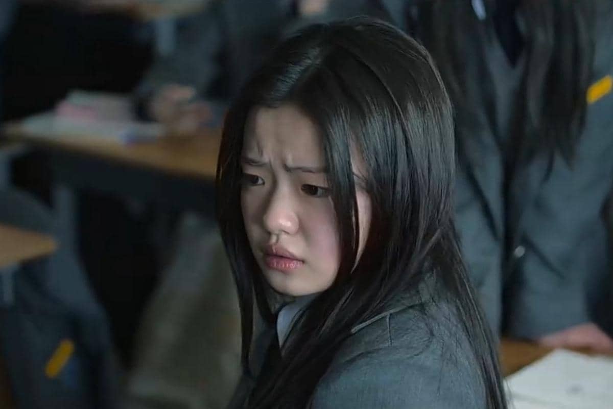 Seorang siswi berseragam abu-abu tampak duduk di kelas dengan ekspresi cemas dalam adegan serial If Wishes Could Kill.