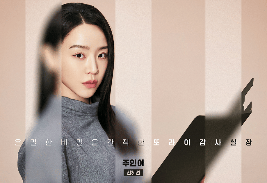 Seorang wanita berambut panjang mengenakan pakaian abu-abu memegang map hitam dalam cuplikan drama Korea Filing For Love.