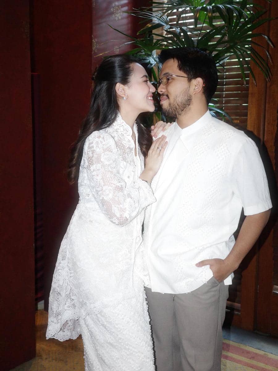 Aaliyah Massaid dan Thariq Halilint mengenakan busana putih saling menatap dan tersenyum hangat di sebuah ruangan dengan latar tanaman hias.