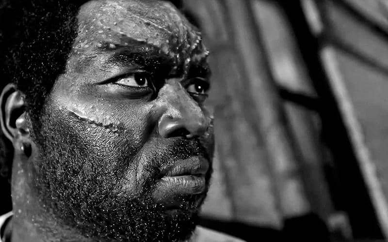 Tombstone dengan wajah penuh bekas luka terlihat serius dalam adegan hitam putih dari serial Spider-Noir di Prime Video.