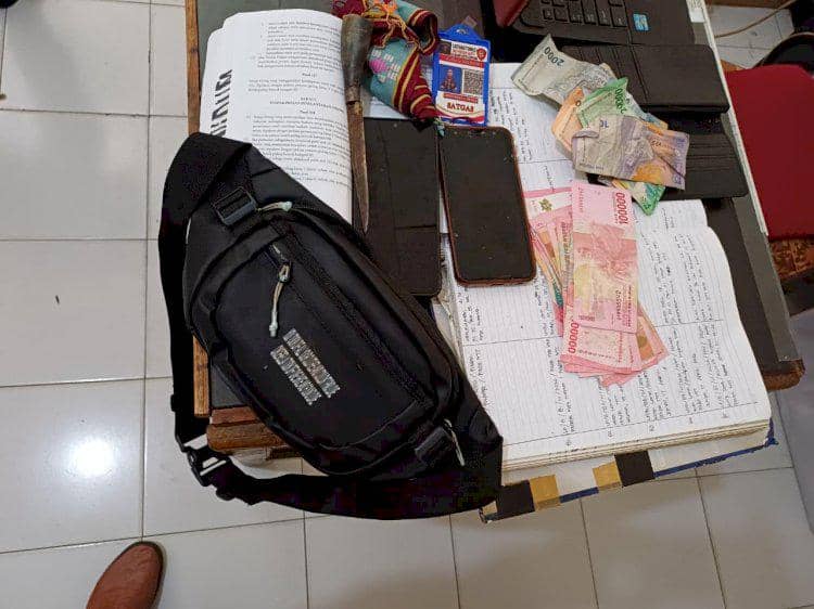 Barang bukti kasus pencurian helm di Kupang berupa tas hitam, uang tunai, ponsel, dan dokumen di atas meja kantor polisi.