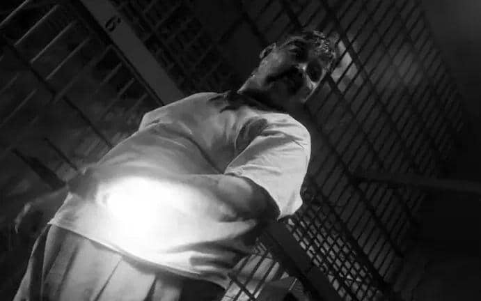 Seorang pria berdiri di depan jeruji besi dengan cahaya terang di perutnya dalam adegan hitam putih dari serial Spider-Noir.