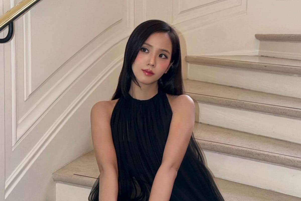 Seorang perempuan berambut panjang mengenakan gaun hitam tanpa lengan duduk di tangga dengan latar dinding berwarna krem.