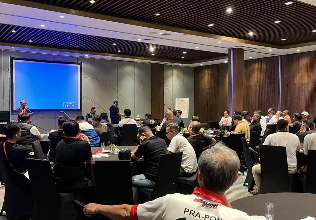 Suasana rapat persiapan Kejurnas ORADO 2026 di Bogor dengan peserta duduk di meja bundar mendengarkan pembicara di depan layar proyektor.