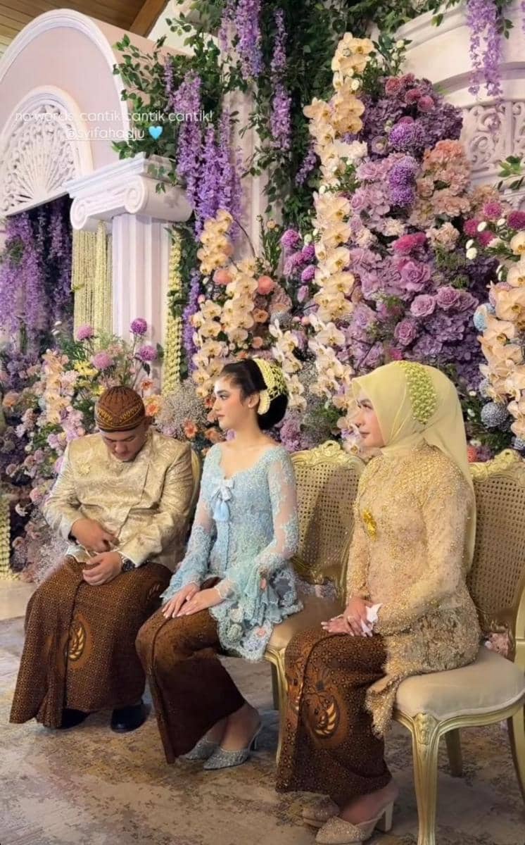 Tiga orang duduk berdampingan mengenakan busana tradisional Jawa di acara pengajian dan siraman dengan dekorasi bunga ungu dan krem.