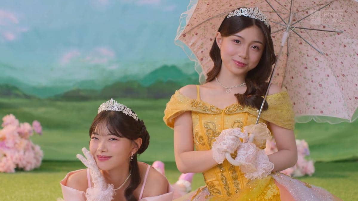 Dua anggota JKT48 Team Love mengenakan gaun bergaya putri dengan mahkota dan payung di latar taman hijau dalam video musik 12 Seconds.