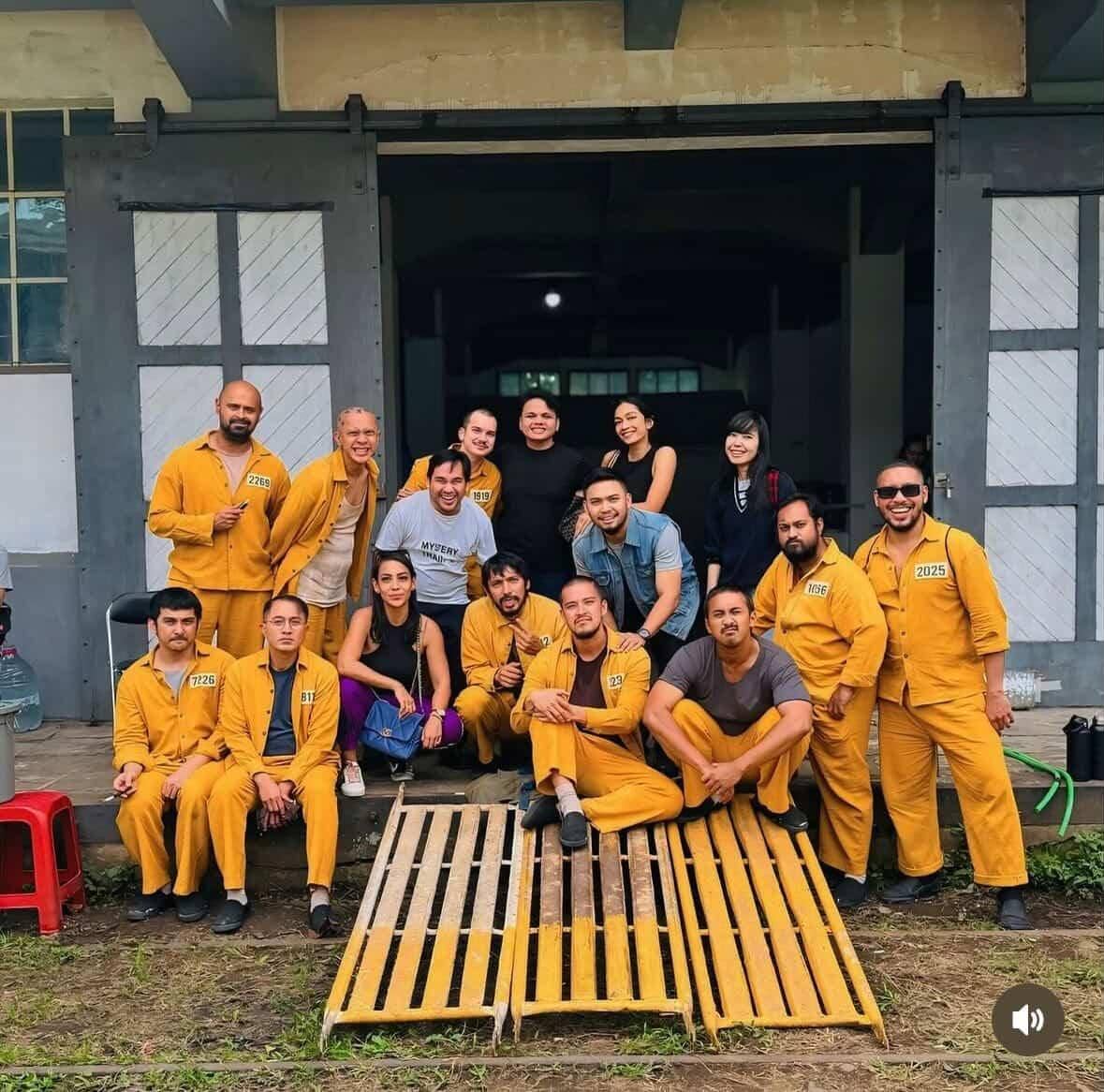 Sekelompok orang berpose bersama di depan bangunan, beberapa mengenakan seragam tahanan berwarna oranye dengan nomor di dada.