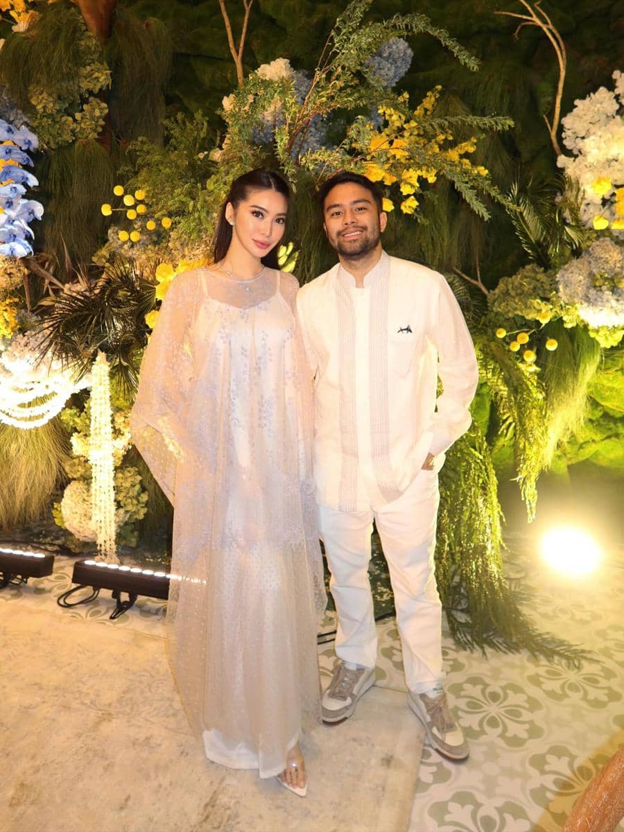 Angie Prijanto dan Ranggaz Laksmana berbusana putih berpose bersama di acara pengajian dan siraman dengan latar bunga dan tanaman hias.