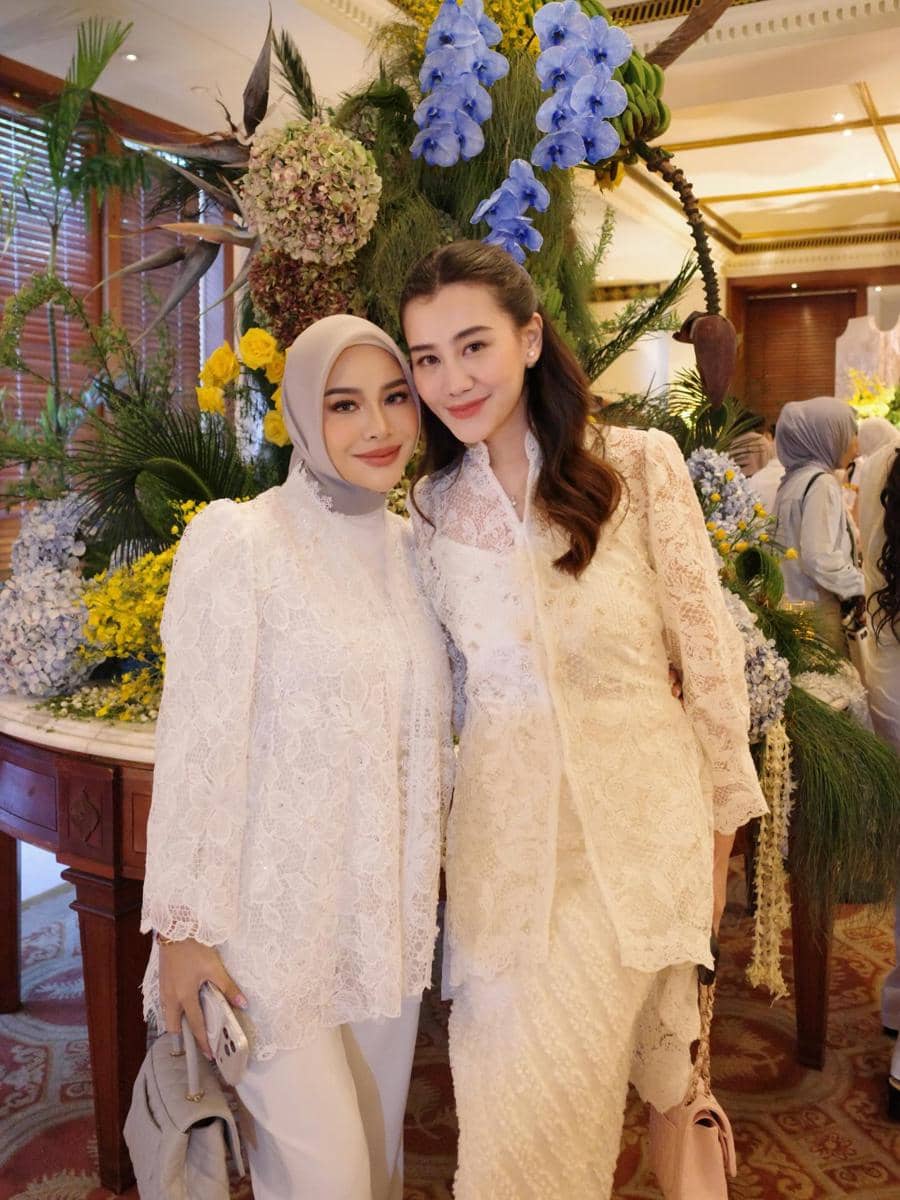 Aurel dan Aaliyah mengenakan kebaya putih berpose bersama di acara pengajian dan siraman dengan latar bunga warna-warni yang indah.
