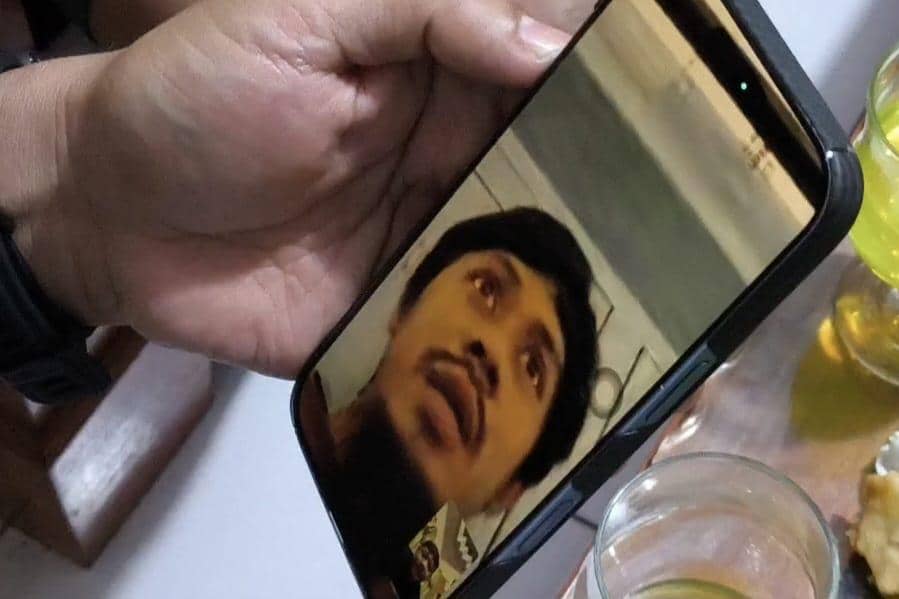 Seseorang melakukan panggilan video dengan seorang pria yang terlihat di layar ponsel, di atas meja terdapat gelas berisi minuman.