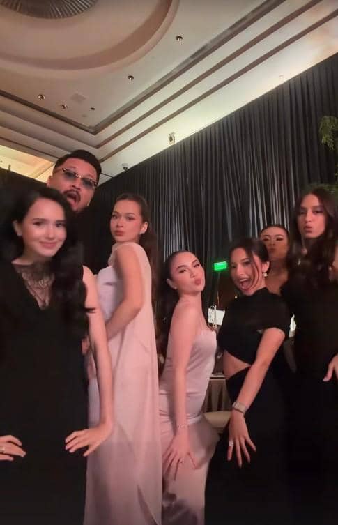 Sekelompok tamu berpakaian formal berpose bersama di resepsi pernikahan dengan latar dekorasi elegan dan pencahayaan hangat.