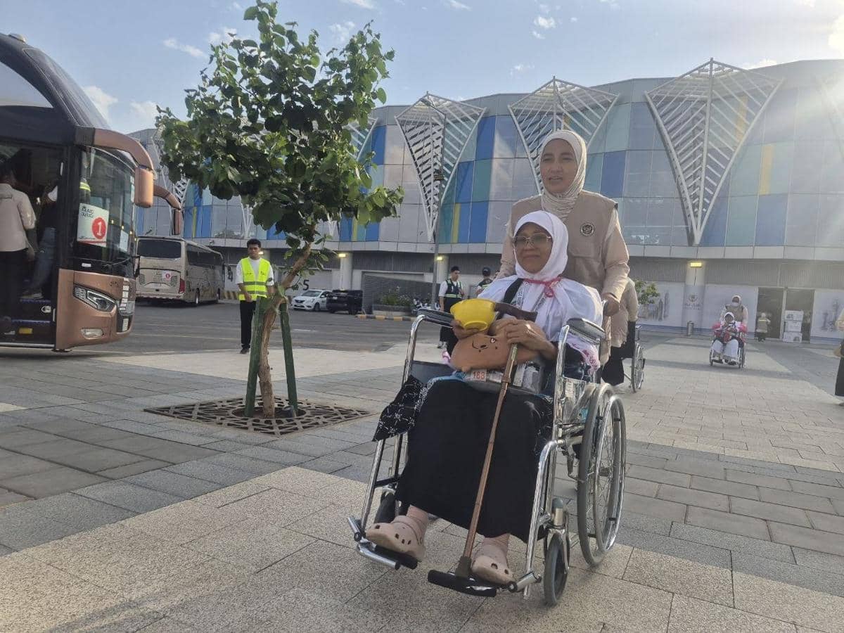 Petugas haji mendorong jemaah lansia asal Kota Malang yang duduk di kursi roda setibanya di Madinah, dengan latar gedung kedatangan modern.