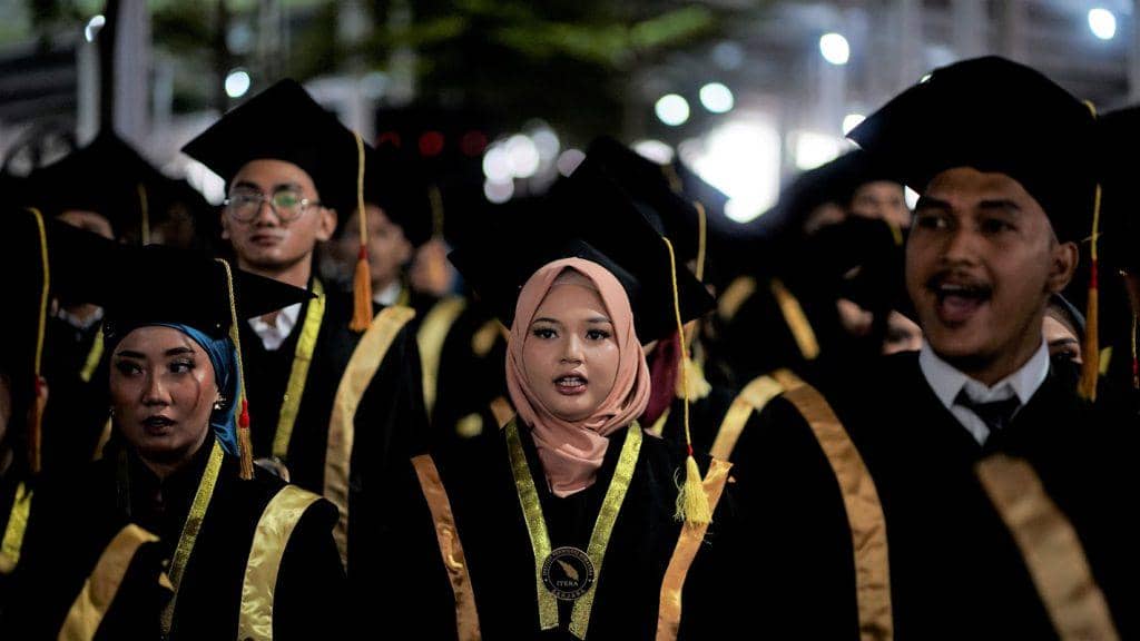 Para wisudawan Institut Teknologi Sumatera mengenakan toga hitam dengan selempang emas saat mengikuti upacara wisuda di pelataran kampus.