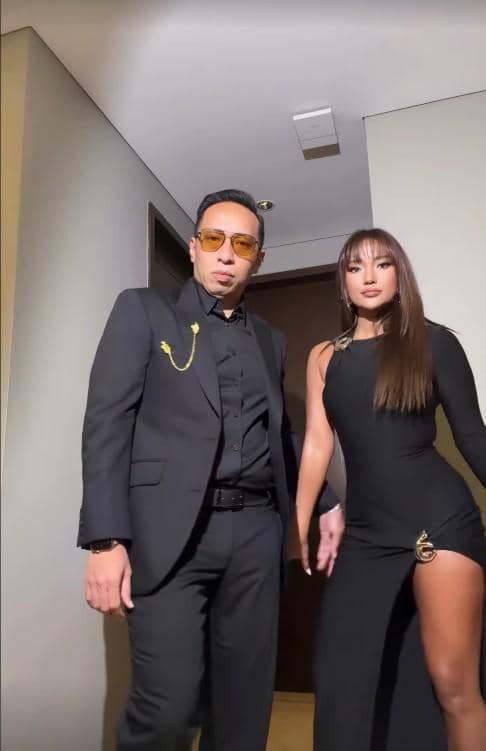 Dua tamu mengenakan busana hitam elegan berpose di lorong sebelum menghadiri resepsi pernikahan El Rumi dan Syifa Hadju.