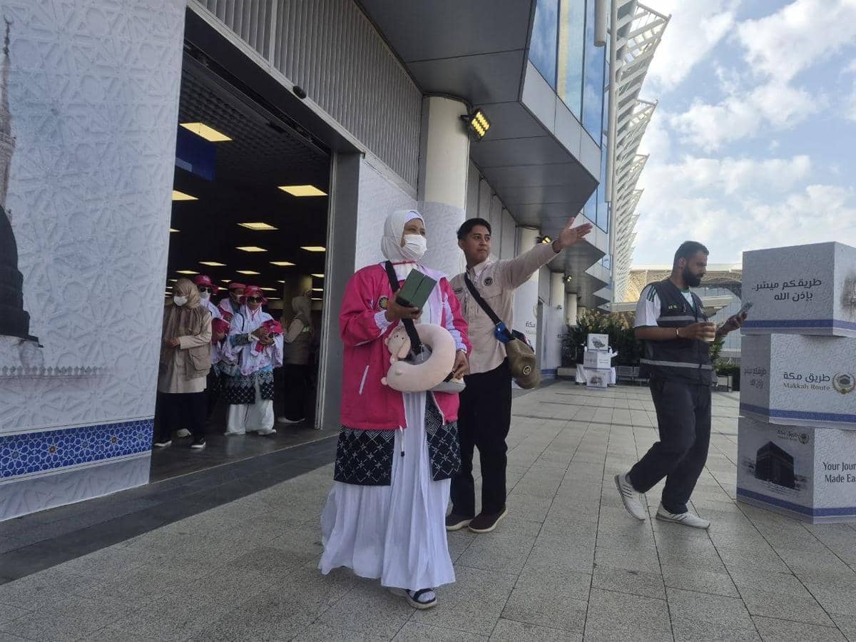 Rombongan jemaah haji asal Kota Malang mengenakan pakaian ihram dan jaket pink tiba di Madinah, dipandu petugas di area kedatangan.