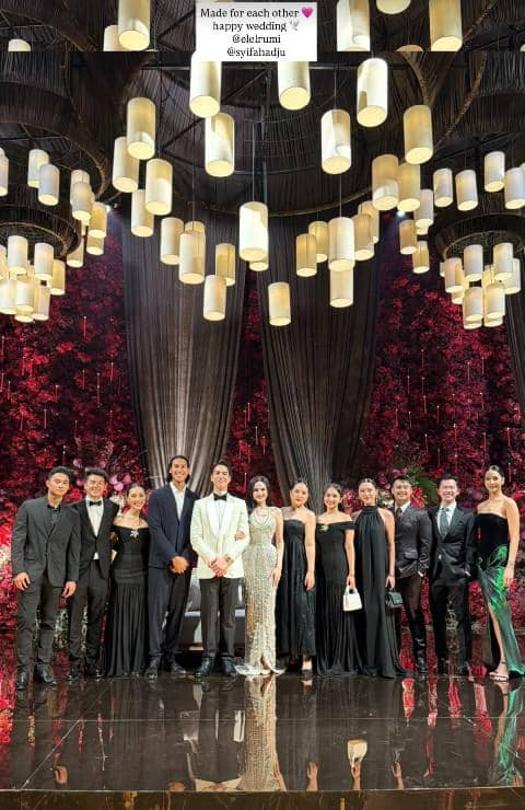 Para tamu artis berpose bersama pengantin di resepsi pernikahan dengan latar dekorasi bunga merah dan lampu gantung elegan.