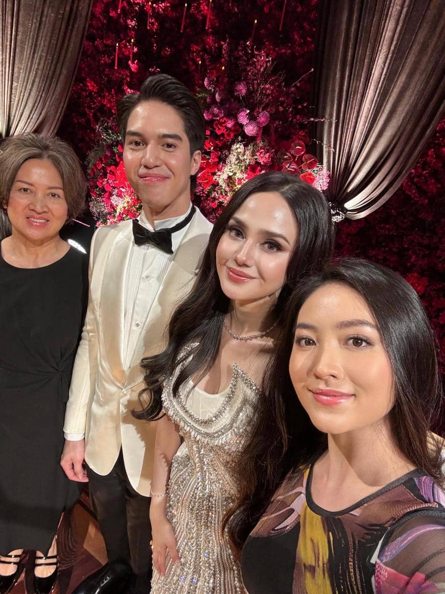 Beberapa tamu berpose bersama di resepsi pernikahan dengan latar dekorasi bunga merah dan pencahayaan hangat yang elegan.