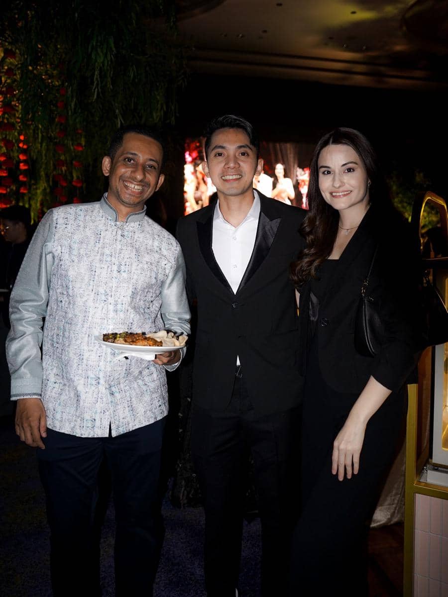 Tiga tamu berpakaian formal tersenyum di resepsi pernikahan El Rumi dan Syifa Hadju dengan latar dekorasi pesta malam hari.
