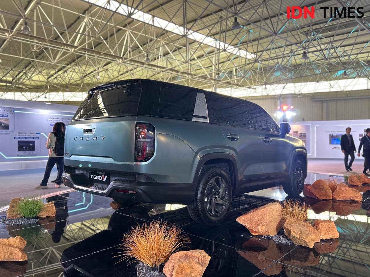 Mobil Chery Tiggo V berwarna abu-abu dipamerkan di dalam ruangan dengan konsep 3-in-1, dikelilingi batu dan tanaman hias.