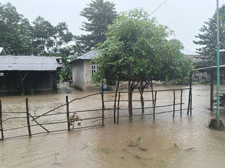Air banjir menggenangi halaman rumah dan jalan di Kabupaten Malaka, Nusa Tenggara Timur, dengan pagar kayu dan pepohonan terendam.