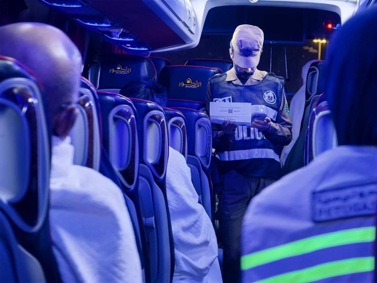 Petugas polisi Arab Saudi memeriksa visa penumpang di dalam bus dengan pencahayaan biru, memastikan dokumen perjalanan sesuai aturan.