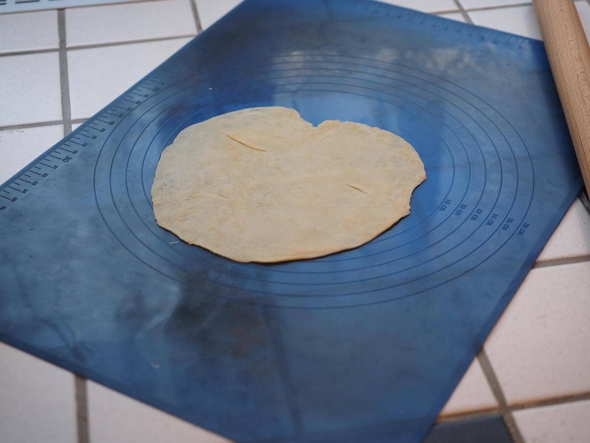 Adonan phyllo tipis berbentuk bulat diletakkan di atas alas silikon biru dengan penggaris dan rolling pin di sampingnya.