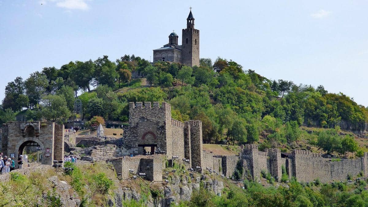 Benteng Tsarevets berdiri megah di atas bukit hijau dengan tembok batu kokoh dan menara gereja di puncaknya pada hari cerah.